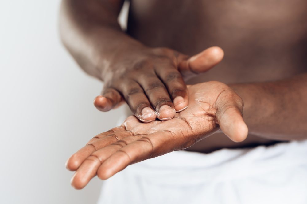 African American man smears hands by moisturizing cream. Hand care. Male beauty concept. Isolated on white background.