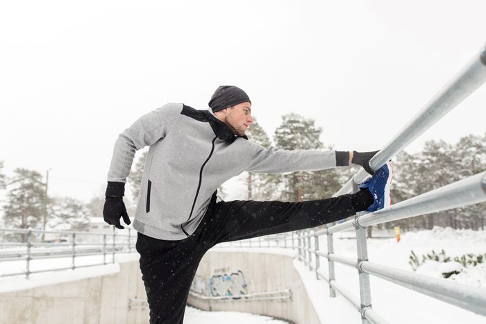 fitness, sport, people, exercising and healthy lifestyle concept - young man stretching leg and warming up at fence in winter