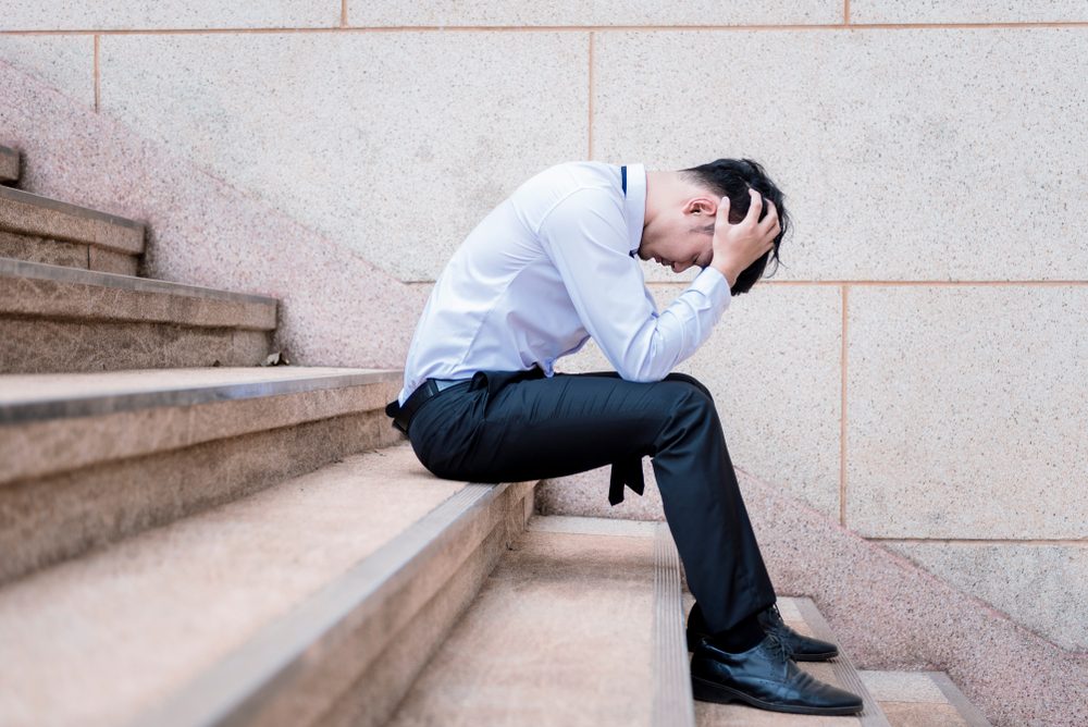 Asian businessman professional failed or upset in his job and sitting on staircase. Business problem concept.