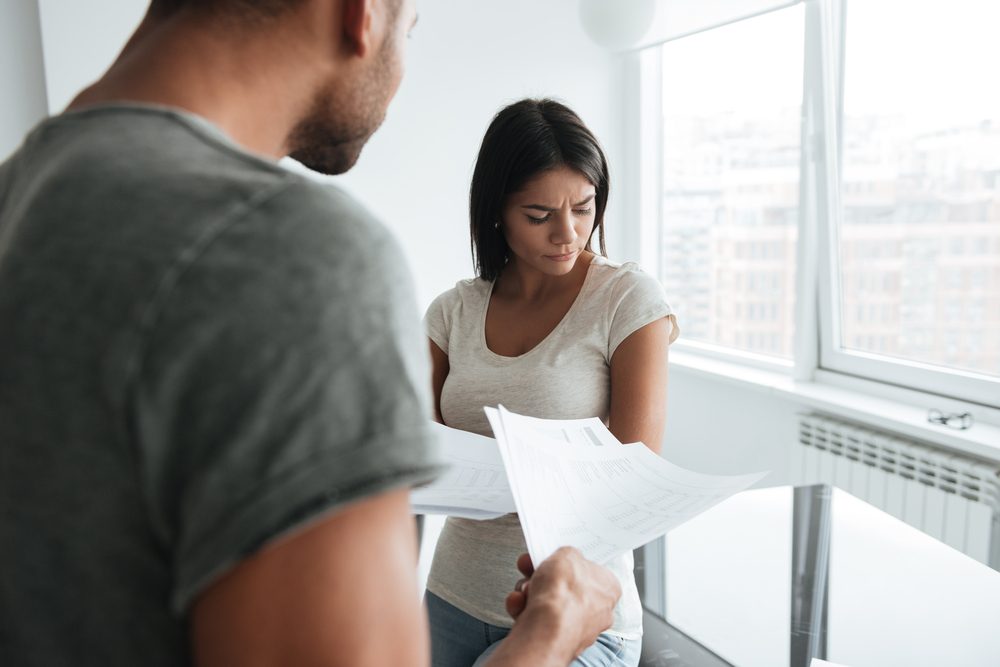 Image of loving couple discussing about domestic bills at home. Sad woman look aside.