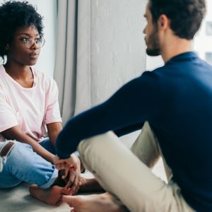 Young African woman and Caucasian man sitting near the window, staring at each other meditating together, free their minds from thoughts and worries.
