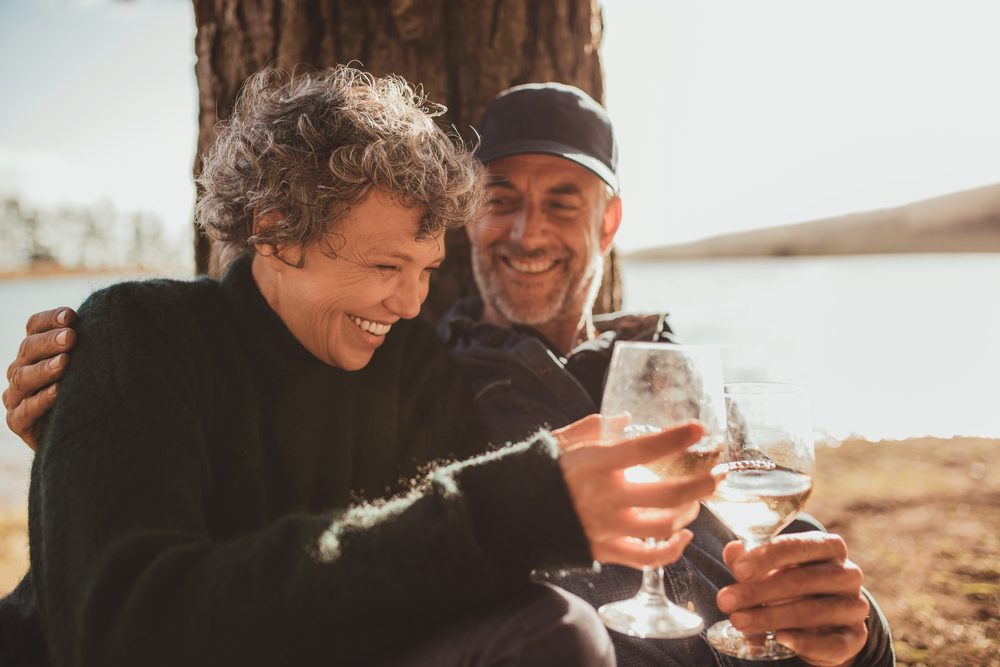 Portrait of relaxed mature couple having a glass of wine at campsite. Senior man and woman toasting wine at on summer day.