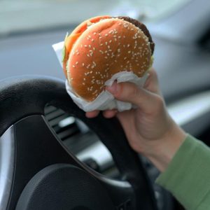 Close up of driver's hand at the wheel while eating food in the traffic