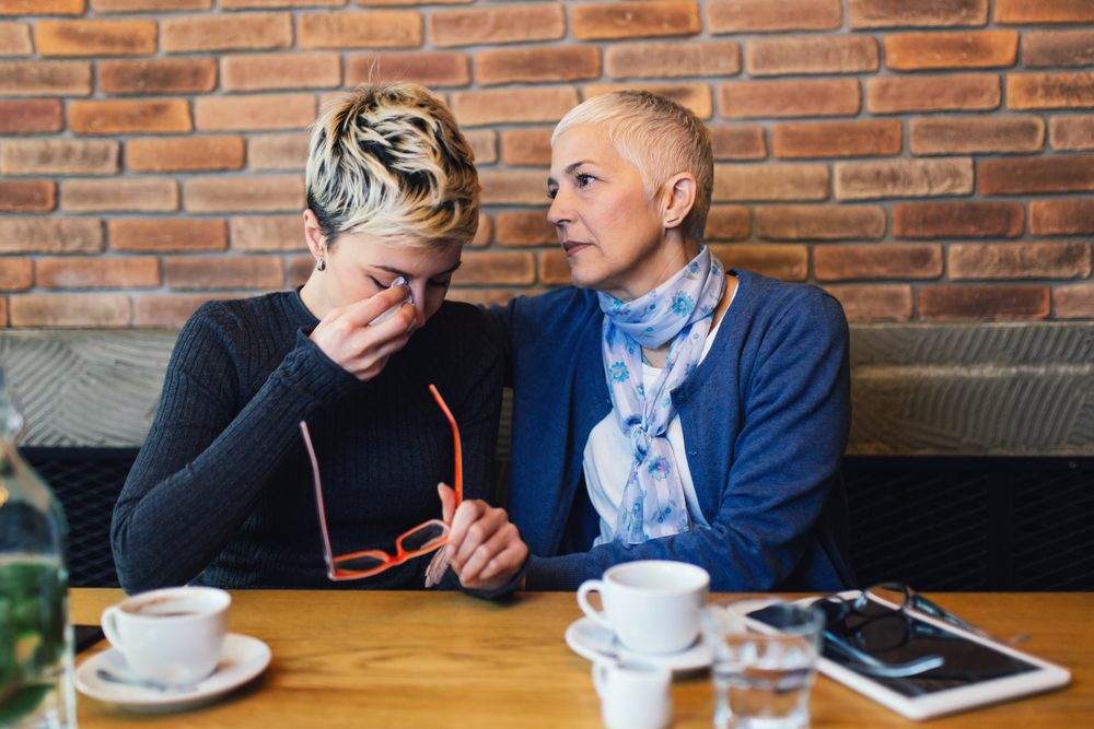 Sad and unhappy daughter sitting in cafe bar or restaurant with her mother and talking.