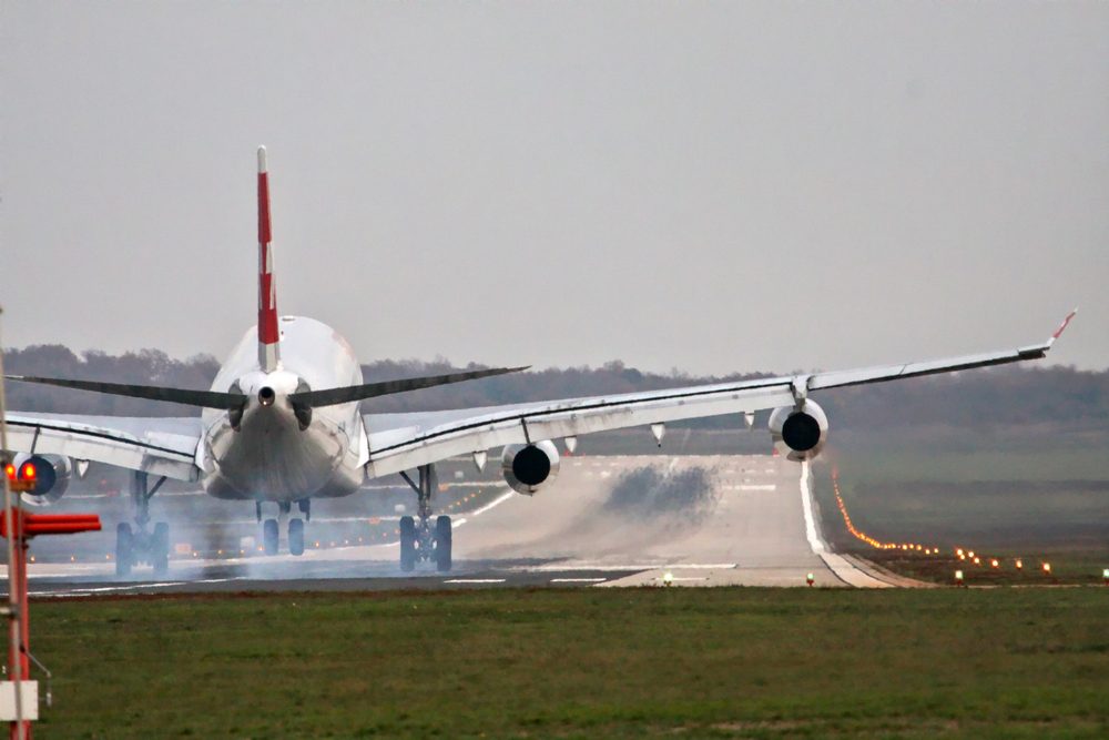 Airplane with four engines landing on runway back view - touchdown with tire smoke