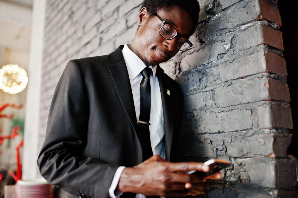 Business african american man wear on black suit and glasses at office looking on mobile phone.