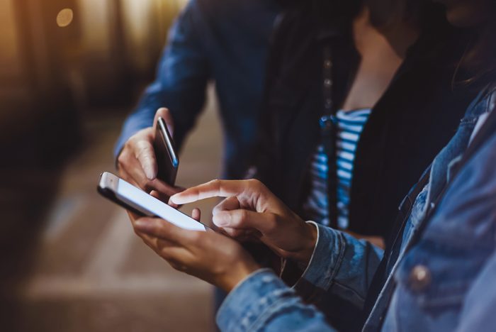 Bloggers together pointing finger on screen smartphone on background bokeh light in night city, group adult hipsters friends using in hands mobile phone closeup, street online wi-fi internet concept