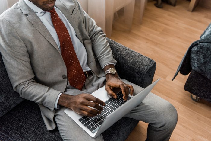 cropped view of african american businessman typing on laptop in hotel room