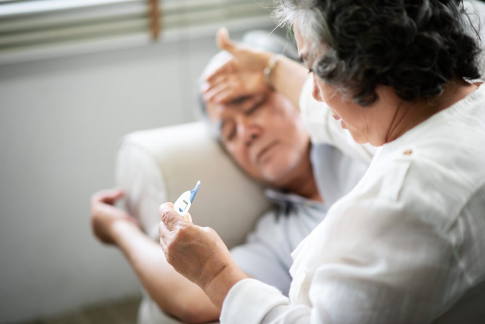 Sick Asian Senior man lying on sofa while his wife holding and looking to thermometer. illness, disease.