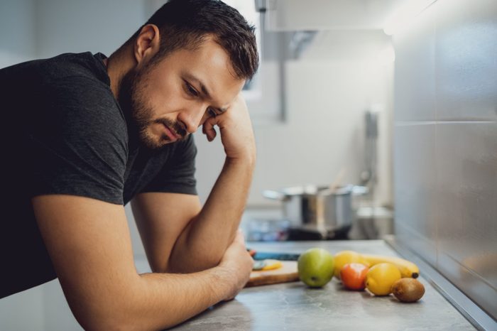 Sad man leaning on the kitchen countertop and looking down