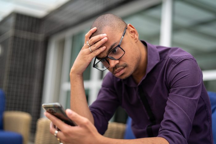 distraught man with his hand on his head looking down at his phone