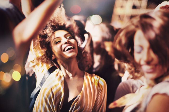 Two young women dancing and jumping at the music festival. They raised their arms and cheer to the music.