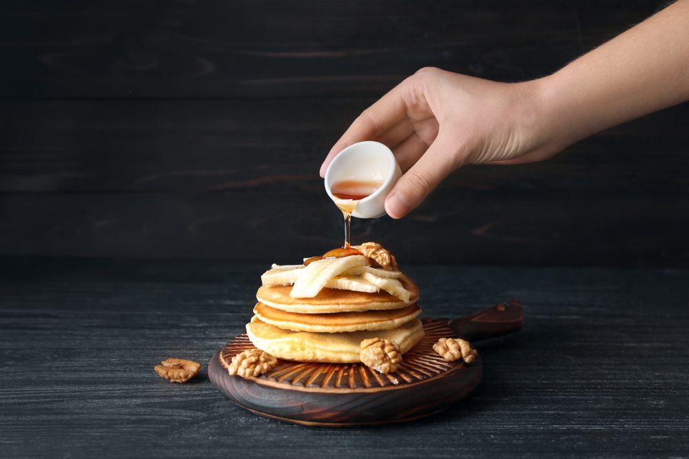 Woman pouring honey onto tasty pancakes