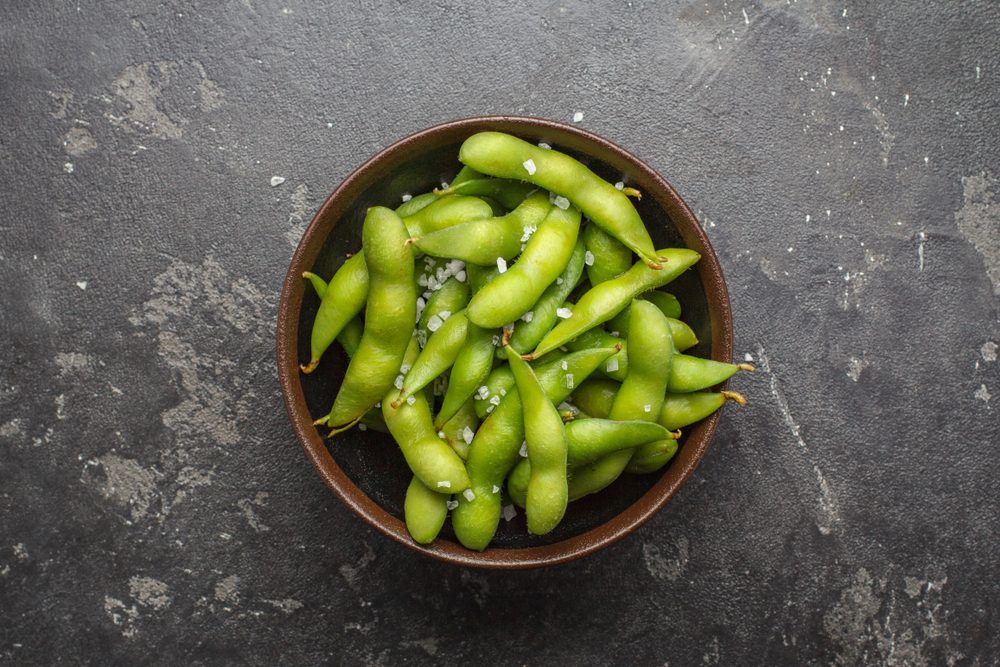 Fresh steamed edamame sprinkled with sea salt on a stone tabletop.