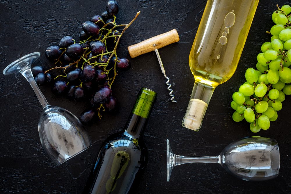 Composition with wine bottles. Red and white wine bottles, bunch of grapes, corkscrew, wine glasses on black background top view