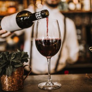 Bartender pouring red wine from a bottle in a wine glass, selective point of view on a wine glass