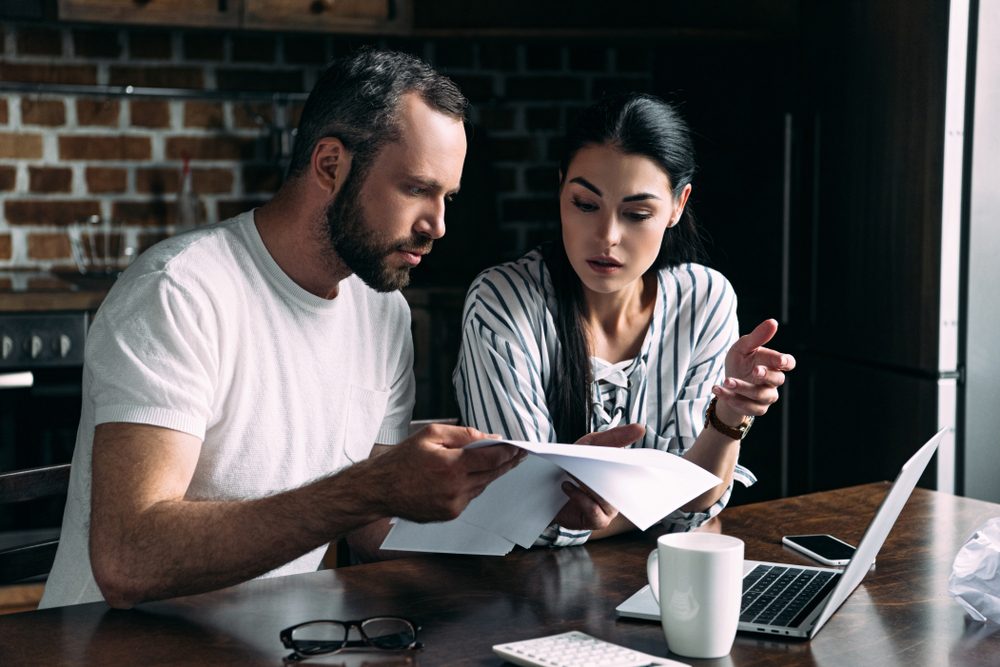 young couple counting bills together on kitchen at home