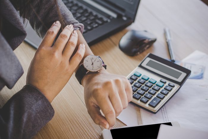 businesswoman boss checking the time on watch waiting for partners coming late sitting at her desk office