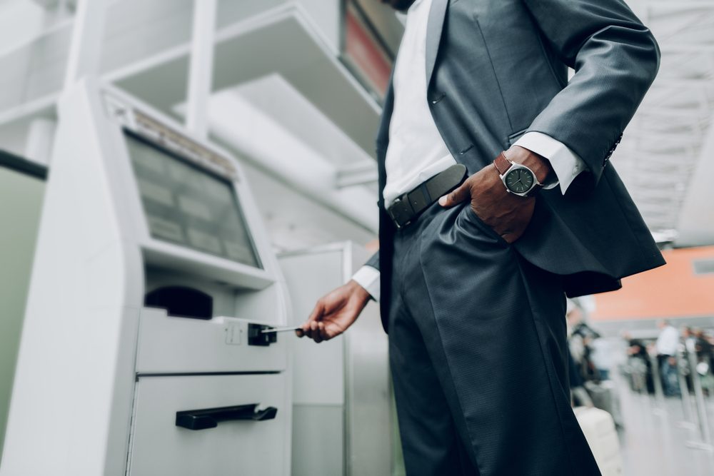 Close up of male is holding hand with watch in his pocket, while standing near cash dispenser