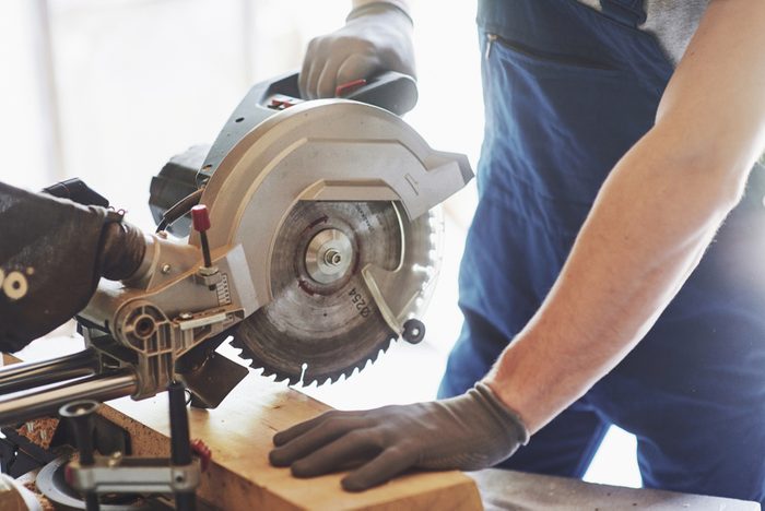 young handsome carpenter working behind a circular saw in the workshop