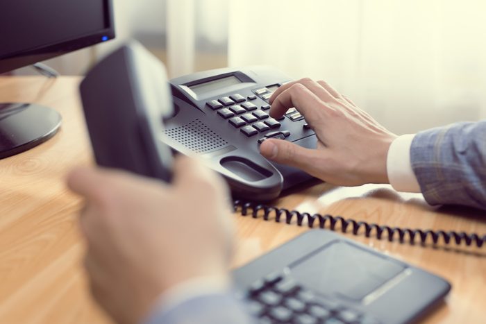 businessman dialing voip phone in the office, keyboard and monitor detail in the background with vintage color tone effect