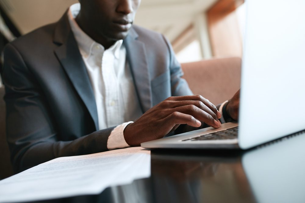 Close up shot of male hands typing on laptop keyboard. African businessman working on laptop computer at cafe.