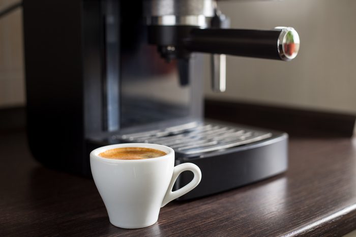 White ceramic cup of espresso with coffee ma?hine on the table. Brewing coffee at work