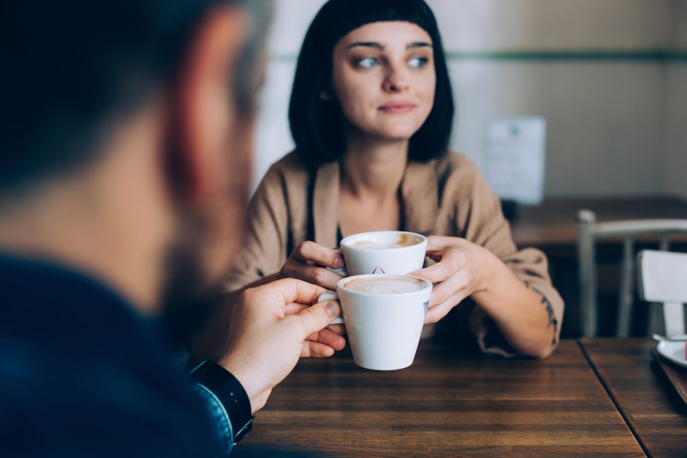 Woman and man, partners of boyfriend and girlfriend are on romantic date getaway in cute adorable cafe, they drink coffee with milk, beautiful girl looks out into window