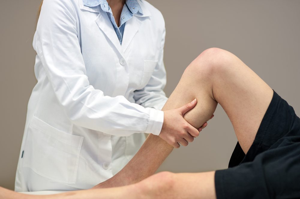 Female doctor physiotherapist practicing massage to her leg male patient in medical center.