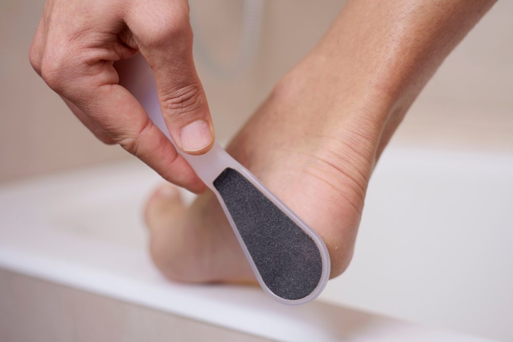 closeup of a young caucasian man in the bathroom using a foot rasp