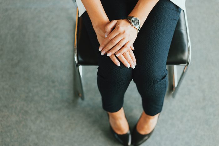 Woman in pants is sitting on the chair. Her arms on the legs. Waiting