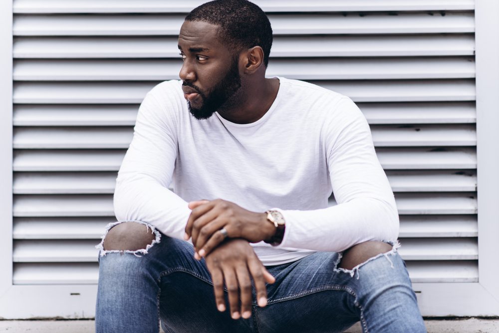 Handsome Afro American man wearing casual clothes in modern city sits near the building