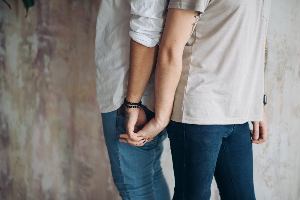 back to back male couple in casual wear, holding hands together, close up