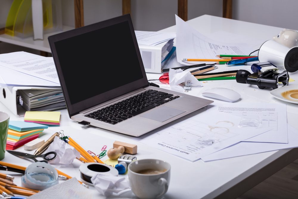 An Open Laptop On The Messy Desk With Coffee Cup And Documents At Workplace