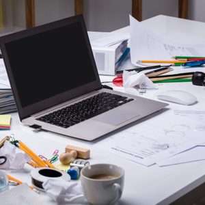 An Open Laptop On The Messy Desk With Coffee Cup And Documents At Workplace