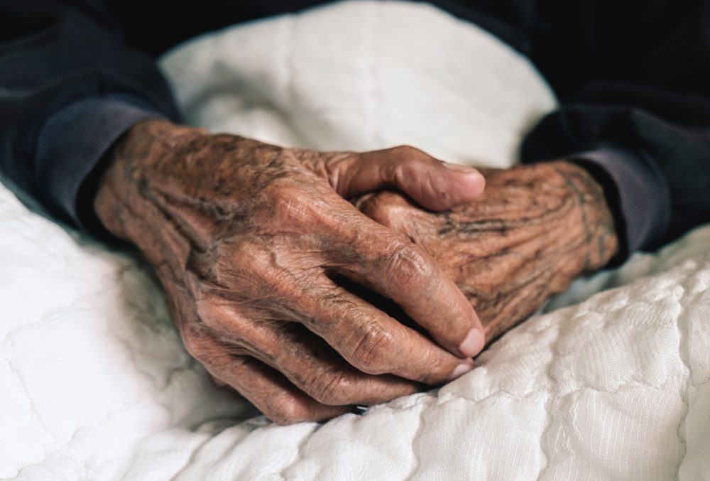 Hands of an old man with wrinkled and wrinkles on a white bed in a hospital.