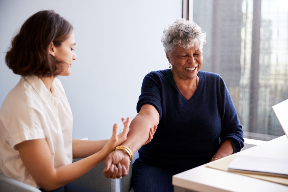 Senior Woman Being Vaccinated With Flu Jab By Female Doctor In Hospital Office