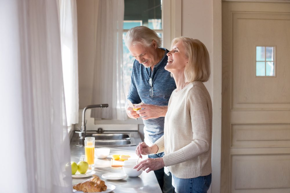 Happy loving senior couple having fun preparing healthy food on breakfast in the kitchen, mature smiling man and woman laughing cooking together on weekend morning, aged old family at home concept