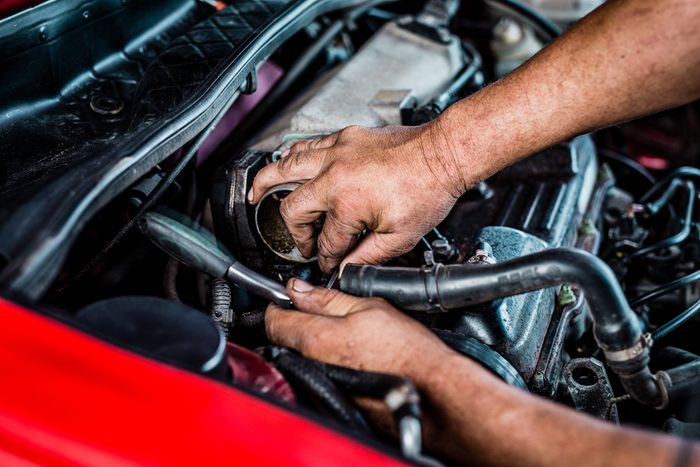 South Afircan mechanic bust working with a racthed spanner inside of a car.
