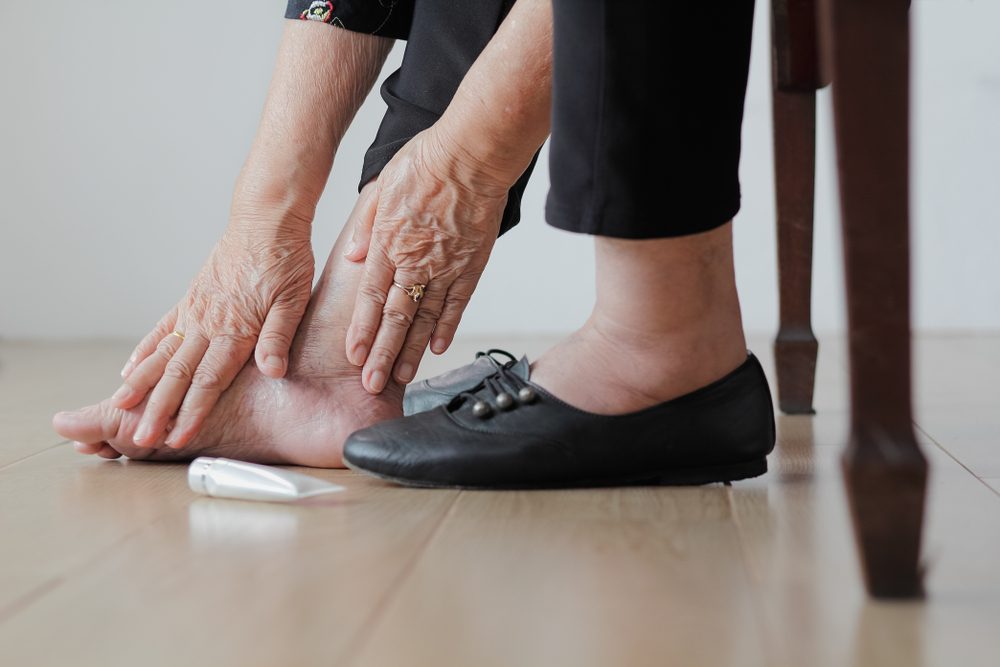 Elderly woman putting cream on swollen feet before put on shoes