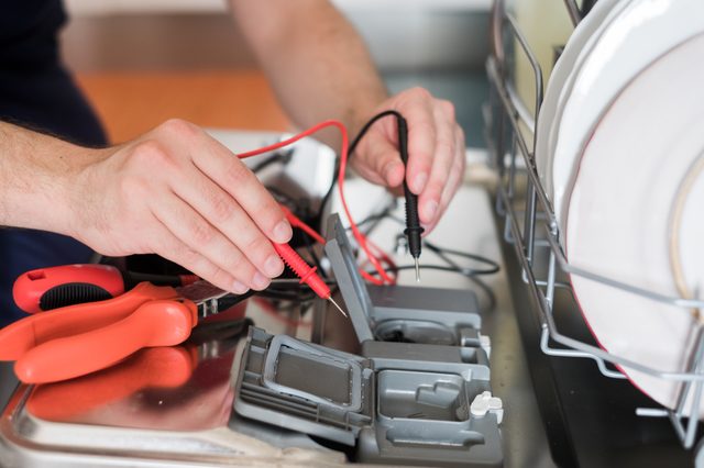 Professional worker repairing the dishwasher in the kitchen