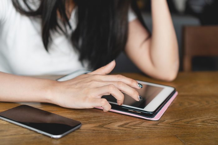 Close up image of young asian woman in casual using digital tablet and smartphone on wooden table in cafe. Business woman reading message and social media on tablet. Device and technology concepts.