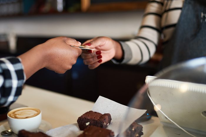 Closeup image of hands of a female african customer giving her bank card to a coffee shop cashier to pay for her cappuccino