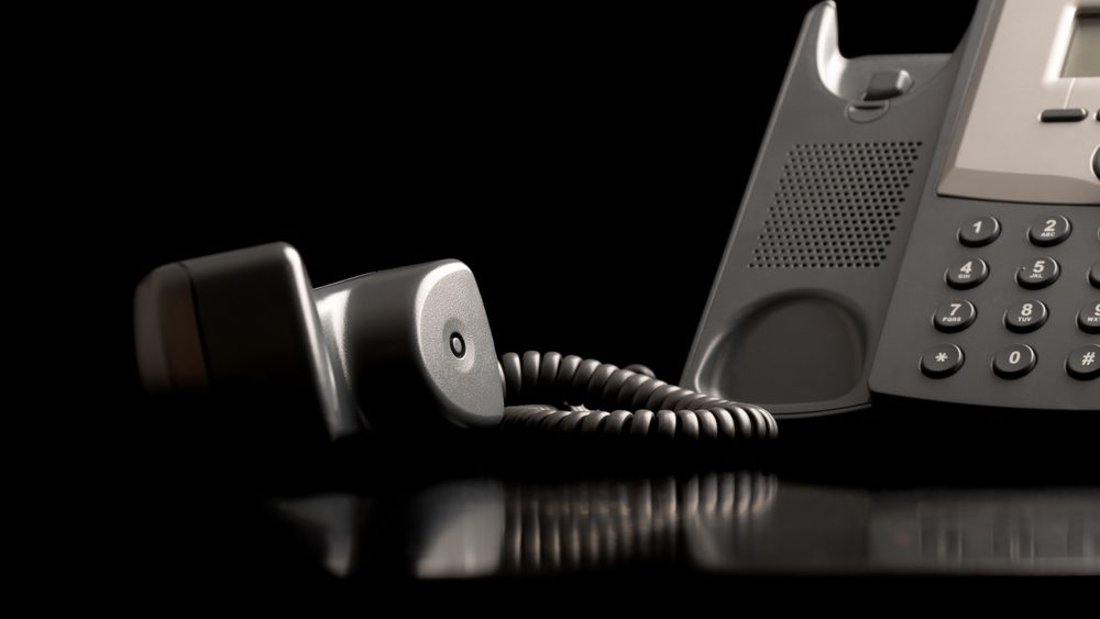 Telephone handset off the hook lying on a black reflective surface alongside the instrument , close up low angle view with copyspace.