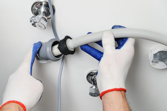 Installation of household appliances. Workman attaches a drain hose to a sewage pipe.
