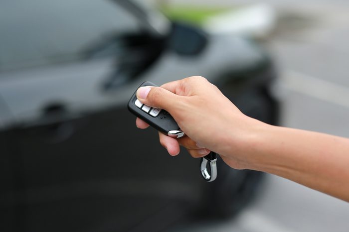 Women hand pressing the button on the remote to lock or unlock the car