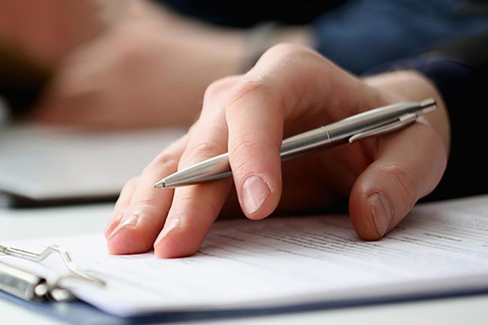 Hand of businessman in suit filling and signing with silver pen partnership agreement form clipped to pad closeup. Management training course, some important document, team leader ambition concept