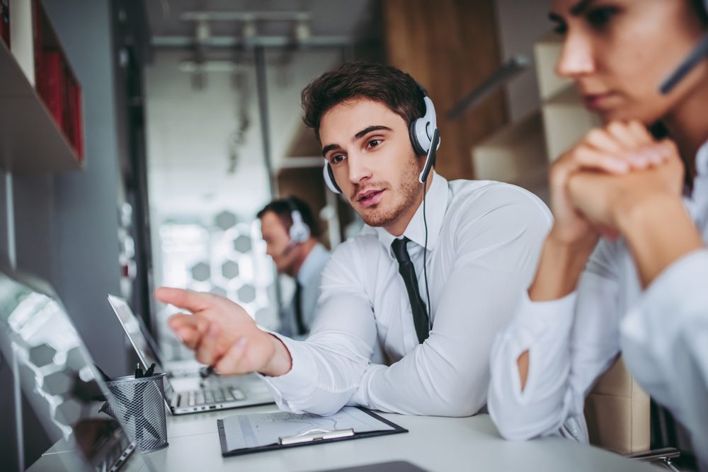 How can I help you? Beautiful call center workers in headphones are working at modern office.