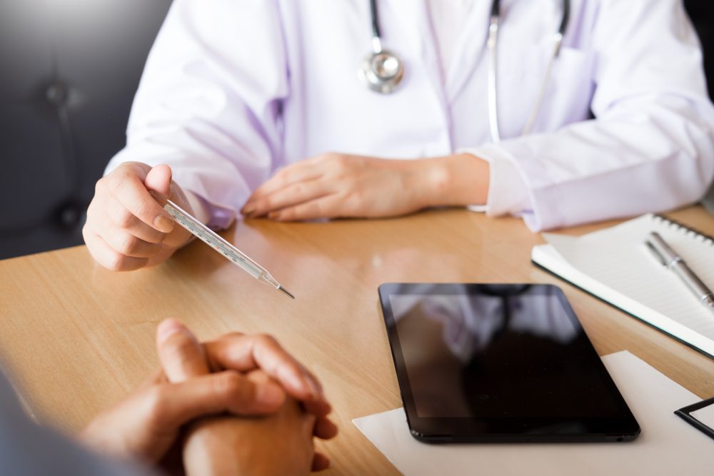 Doctor with a thermometer in his hand taking patient's in hospital, medical concept 