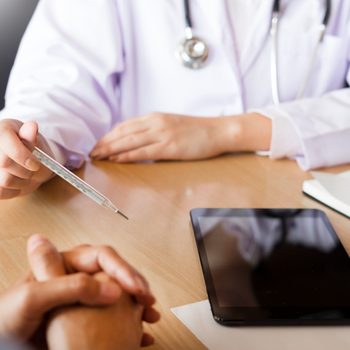 Doctor with a thermometer in his hand taking patient's in hospital, medical concept